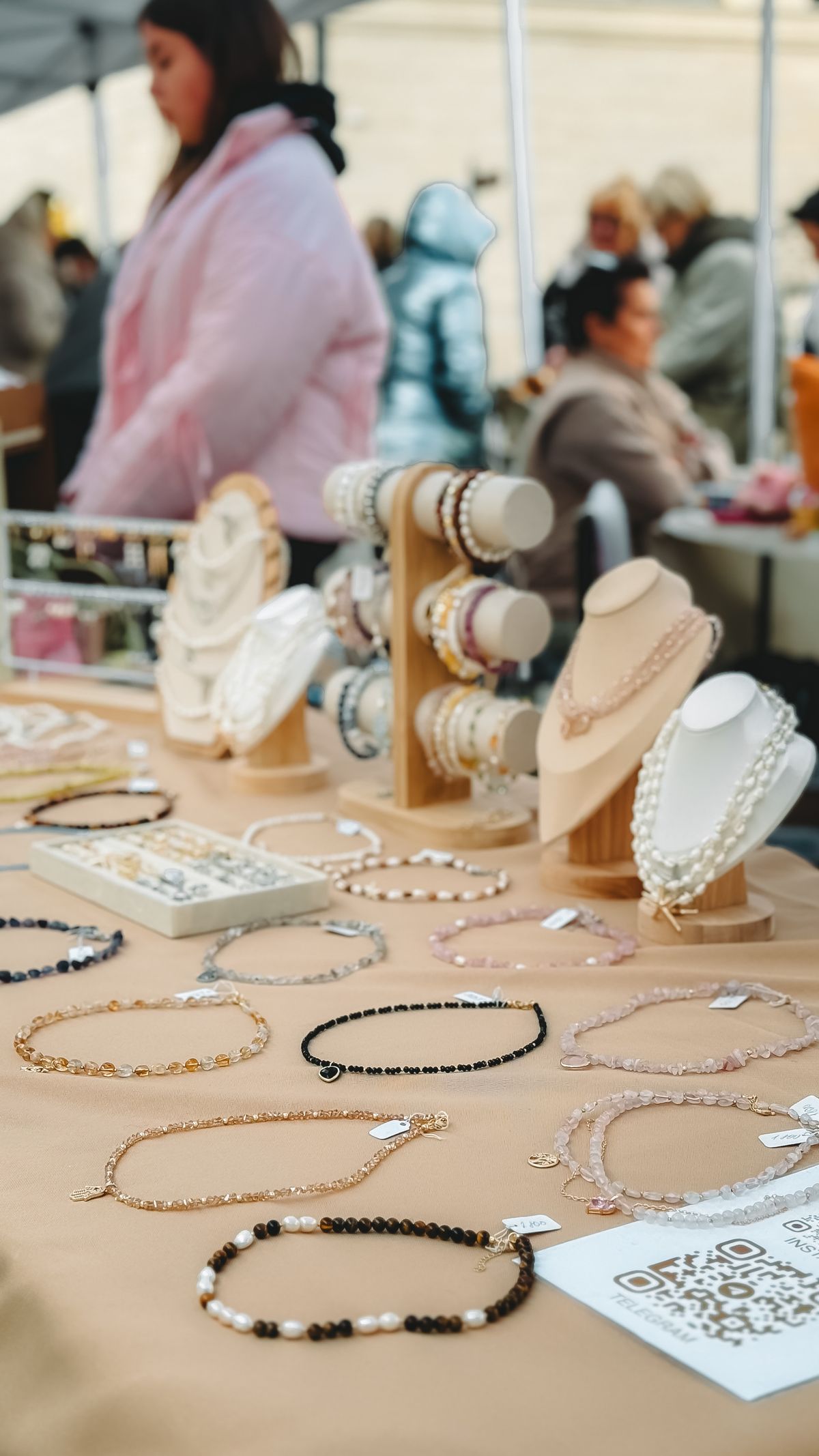 Shoppers in everyday summer clothes browsing a jewelry stall at an outdoor market